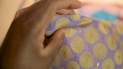 A hand pinches purple and gold printed fabric